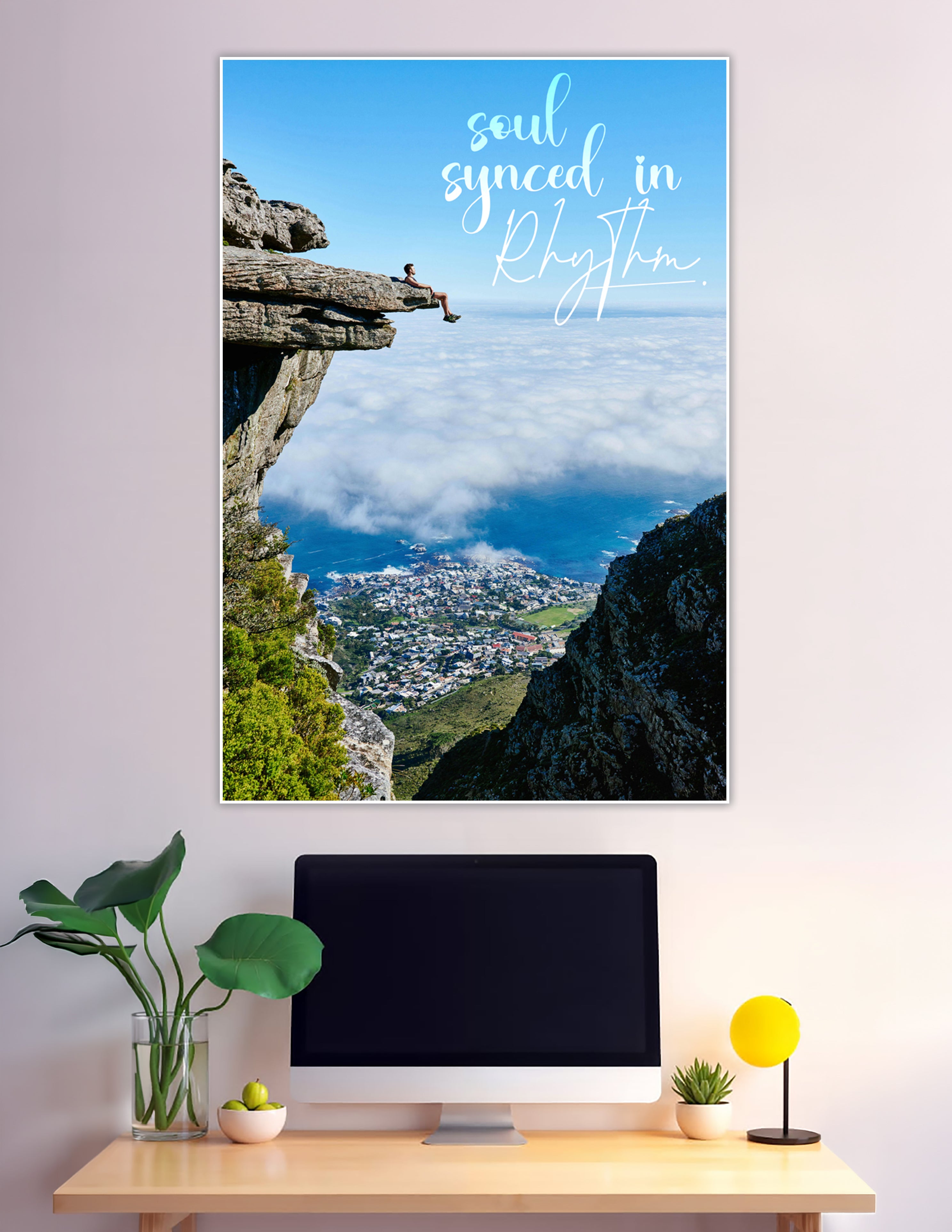 Person sitting on a rocky cliff overhang above clouds overlooking a coastal city with the quote soul synced in rhythm printed on the poster
