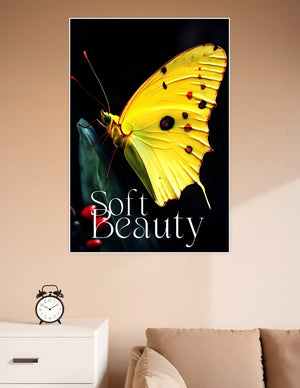 Close-up macro poster of a vivid yellow butterfly with red and black markings perched on a dark green leaf against a black background, titled Soft Beauty