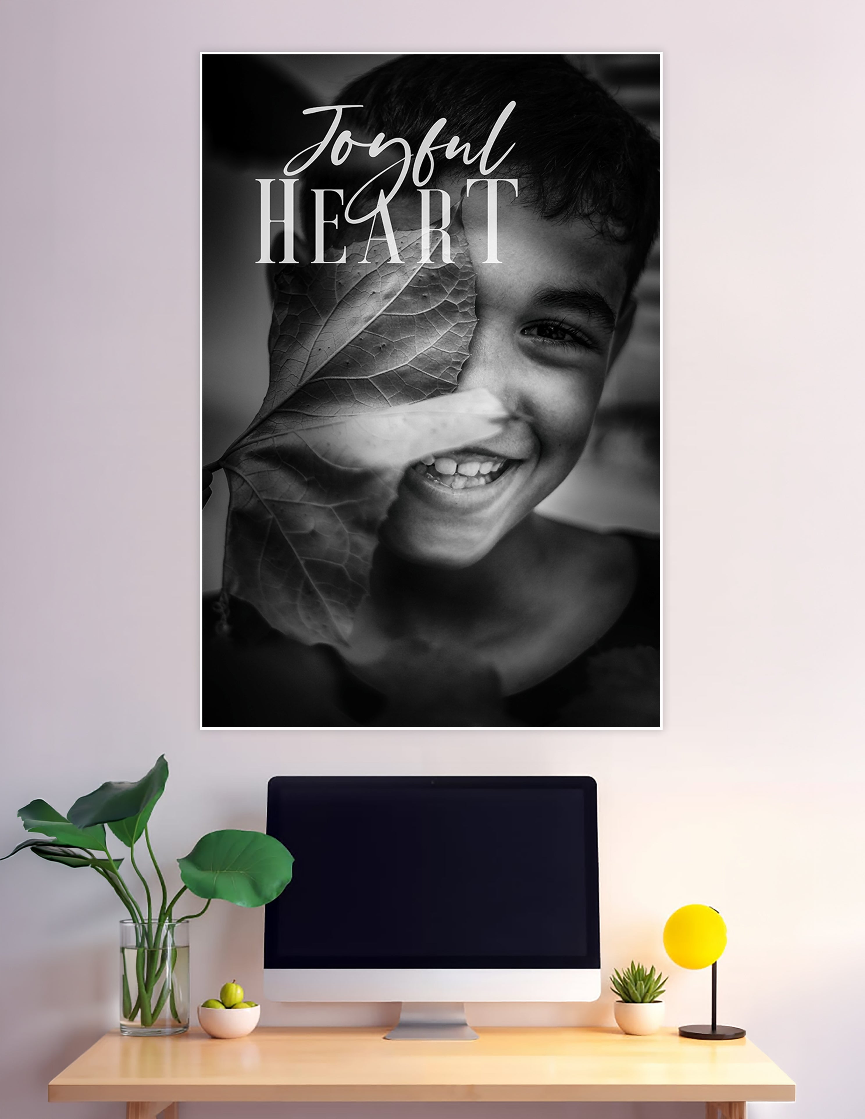 Black and white poster of a smiling child holding a large leaf over their face with 'Joyful Heart' script and serif typography overlay