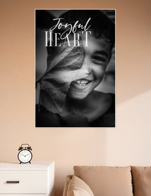 Black and white poster of a smiling child holding a large leaf over their face with 'Joyful Heart' script and serif typography overlay