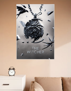 The Witcher official poster featuring the iconic Wolf Medallion shattering apart on a chain against a grey background with the title text below